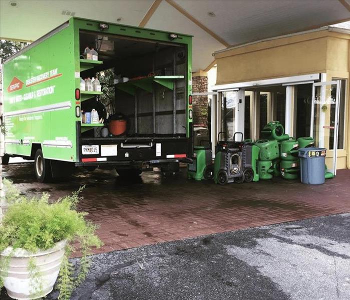 A green SERVPRO truck is shown in front of a commercial site with restoration equipment