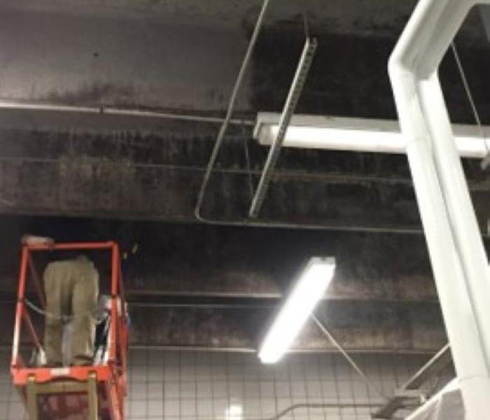 A SERVPRO technician is shown on a lift cleaning an industrial ceiling